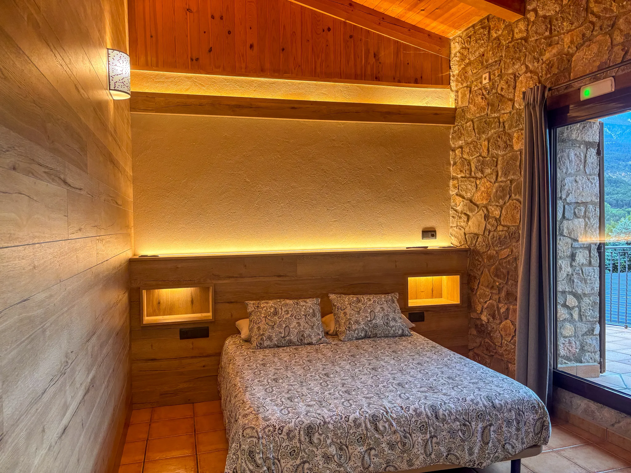 Habitació de la casa rural amb paret de pedra, fusta i vistes a la muntanya