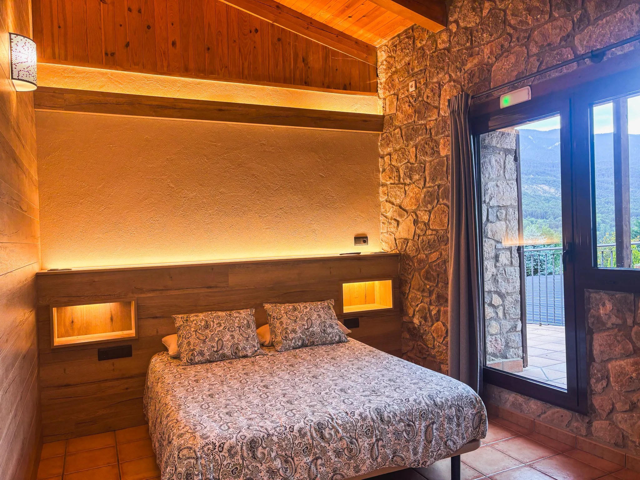 Habitació de la casa rural amb paret de pedra, fusta i vistes a la muntanya
