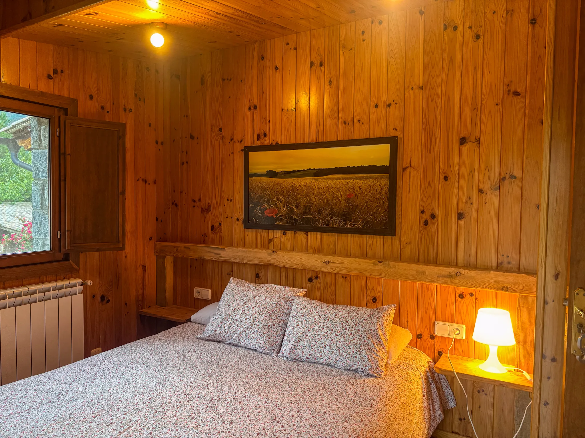 Habitació revestida de fusta amb llit de matrimoni, llum de tauleta i finestra