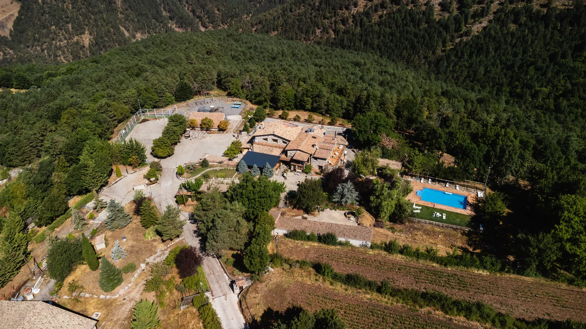 Vista aèria de la casa, la piscina i els camps, envoltats de bosc