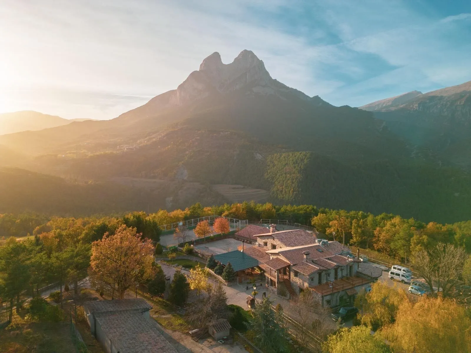 Vista aèria de la casa al capvespre, amb la llum daurada i el Pedraforca al fons