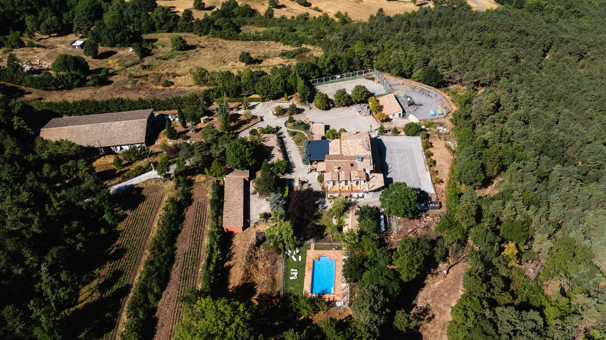 Vista aèria de la casa, la piscina i els camps de conreu, entre el bosc