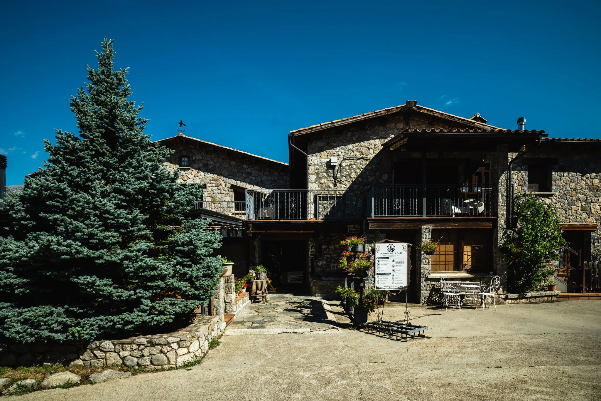La façana de pedra i l'entrada de la casa, amb un gran avet al costat