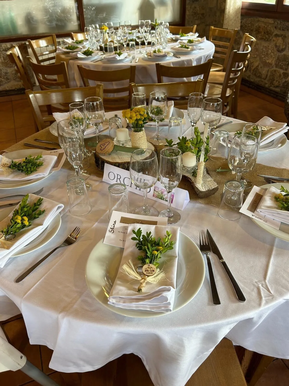 Taules rodones parades per a un casament, amb centres de fusta, espelmes i flors grogues