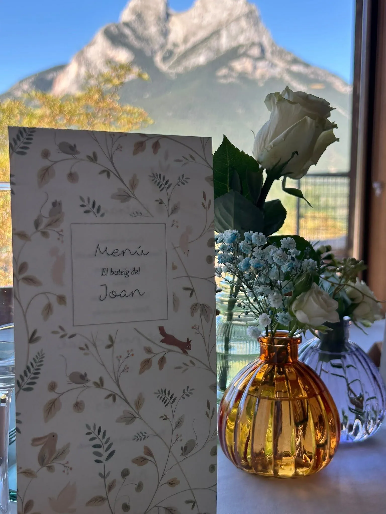 Carta de menú i gerros amb roses blanques sobre la taula, amb el Pedraforca al finestral