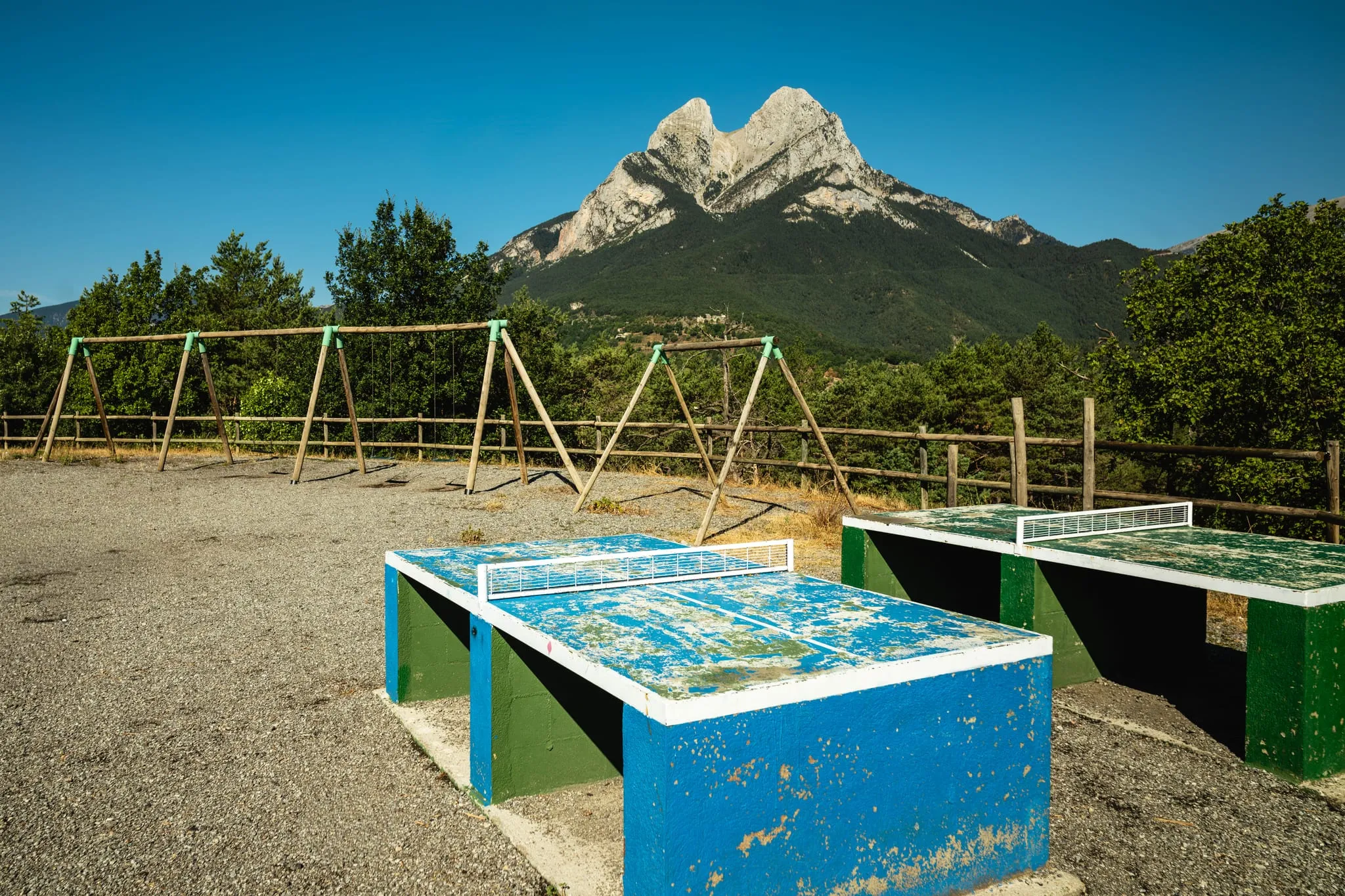 Taules de ping-pong i gronxadors a l'aire lliure, amb el Pedraforca al fons