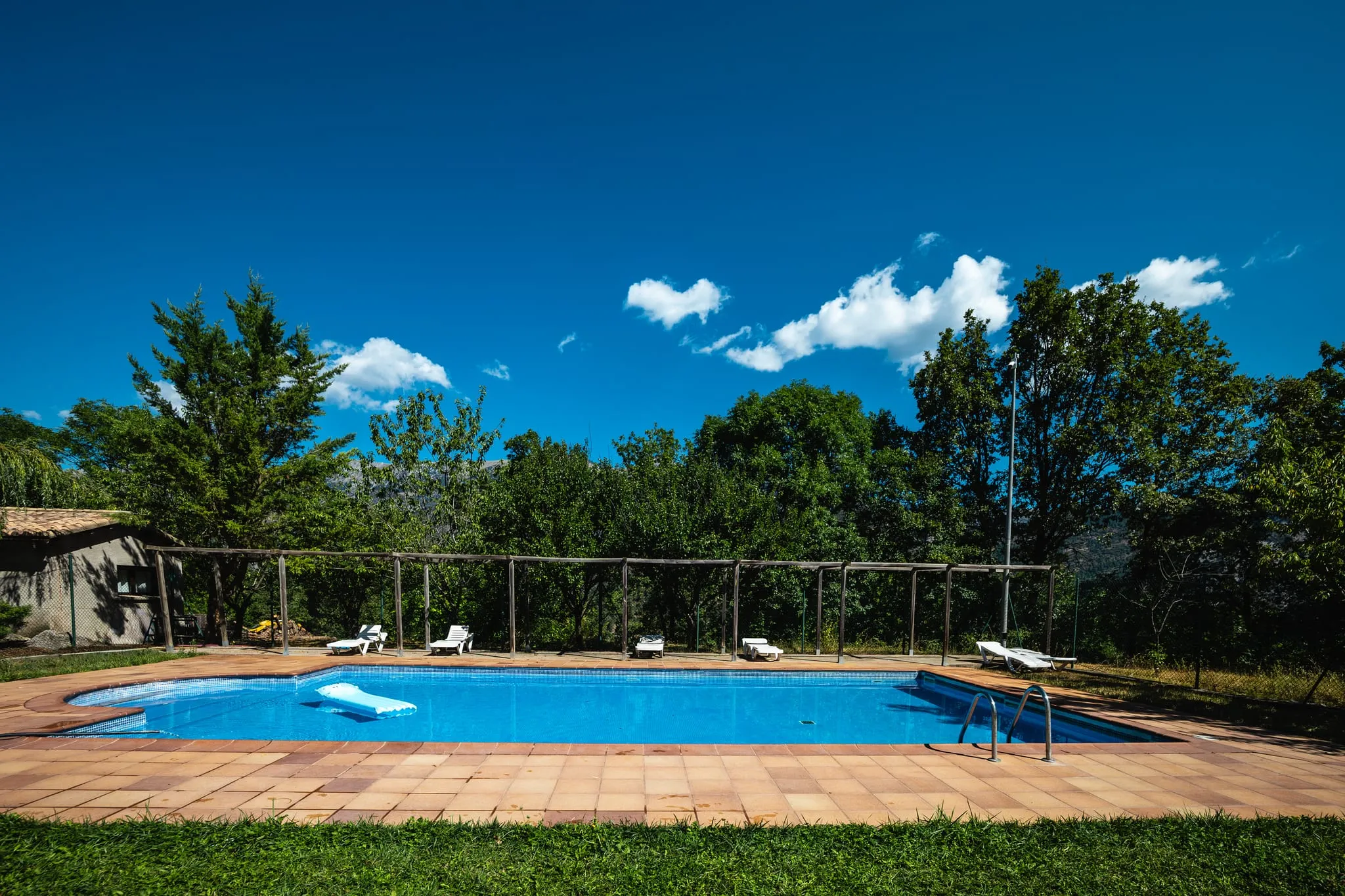 La piscina i la gespa amb gandules, sota un cel blau amb alguns núvols