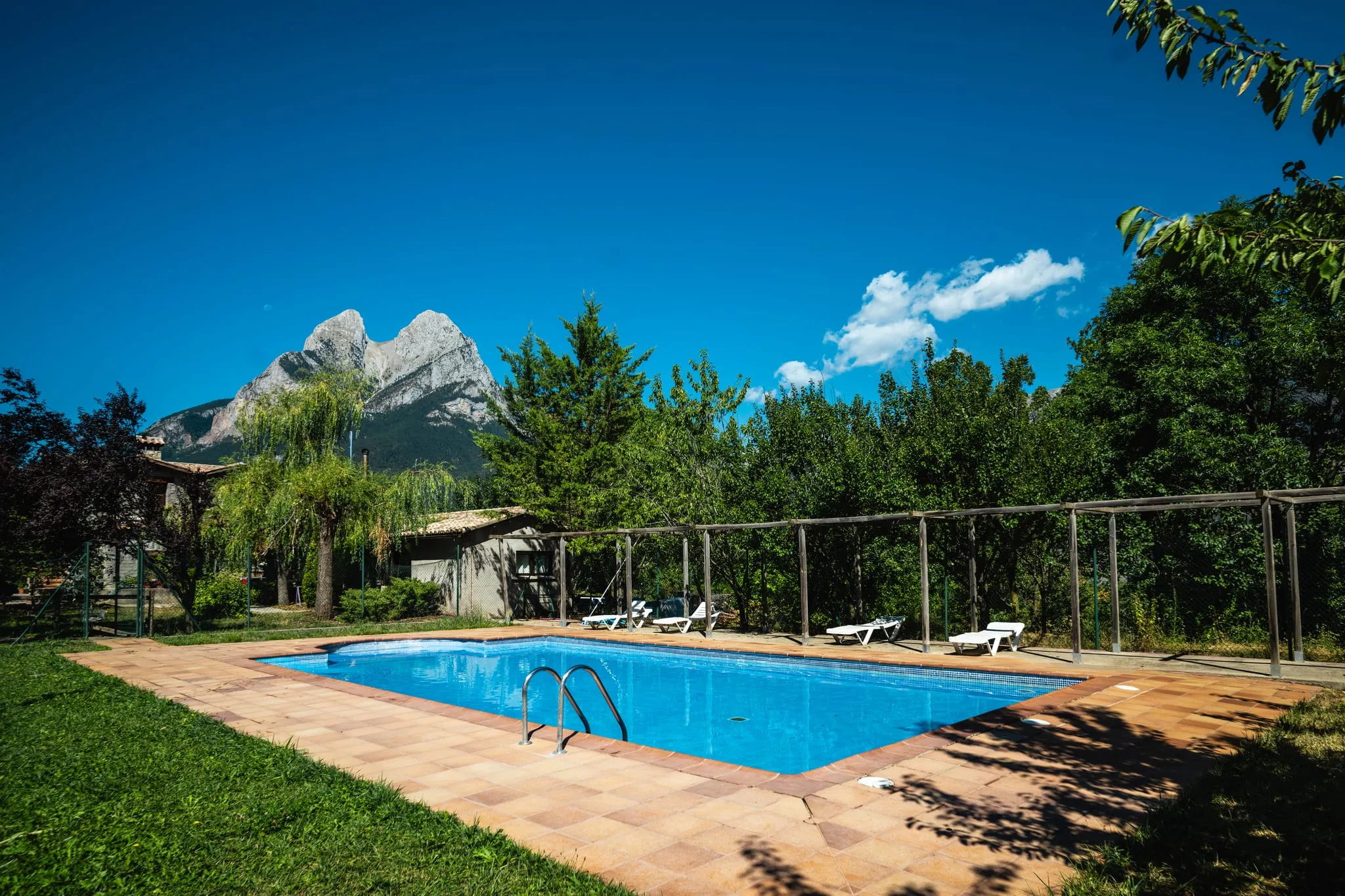 La piscina amb gandules i arbres, i el Pedraforca que treu el cap al fons