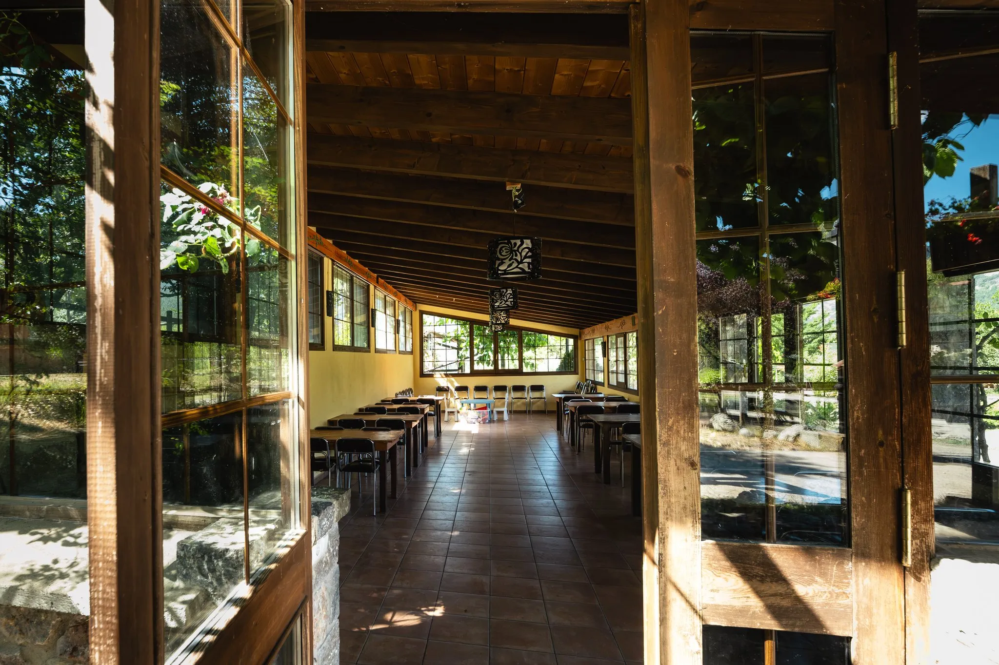 La sala envidrada de la casa, amb taules de fusta i sostre de bigues, vista des de les portes obertes